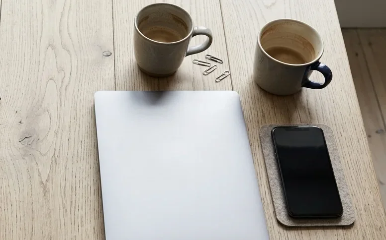 A meeting table after a meeting: two coffee cups, a closed laptop and a phone.